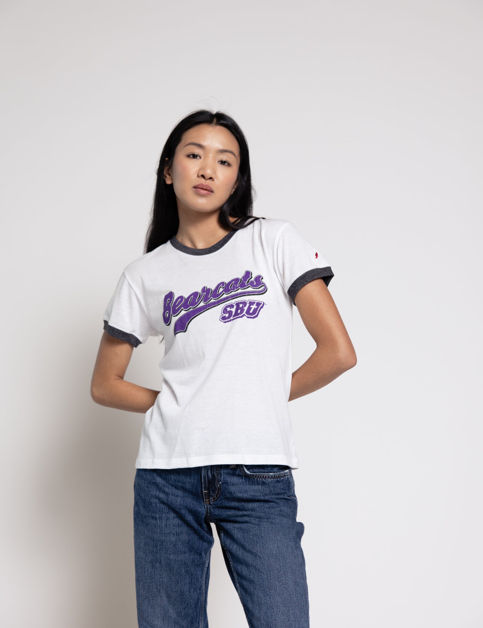 Woman wearing a white t-shirt with purple text and blue jeans on a plain background