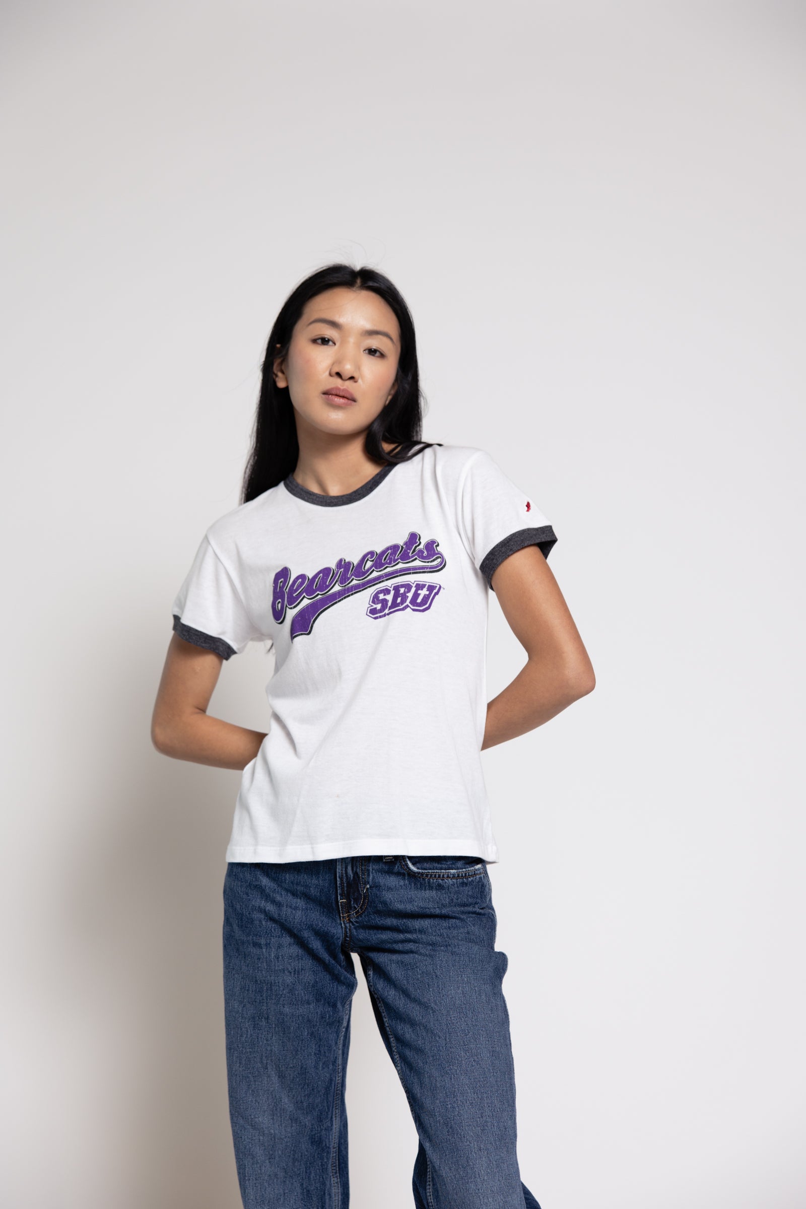 Woman wearing a white t-shirt with purple text and blue jeans on a plain background